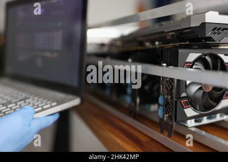 Master in rubber gloves holding laptop in front of mining farm closeup Stock Photo