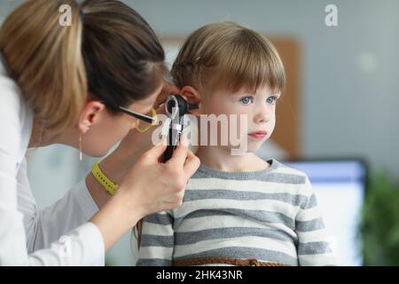 Female pediatrician looking at ear of little girl using otoscope in clinic Stock Photo