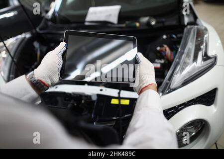 Master repairman holding digital tablet near open hood of car closeup Stock Photo