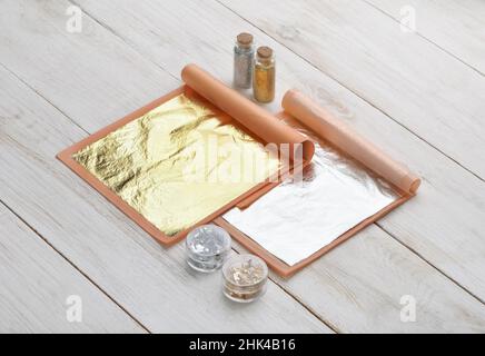 Natural edible food gold and silver sheets, flakes and powder on white wooden table Stock Photo