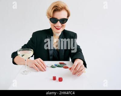 mature stylish woman in black tuxedo and sunglasses happy to win in casino. Gambling, fashion, hobby concept. Stock Photo