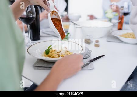 cropped view of woman pouring bolognese sauce in pasta with grated cheese on plate Stock Photo