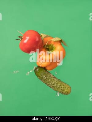 Flying group of vegetables-pepper, cucumber, tomato on a green background. Still life of vegetables Stock Photo