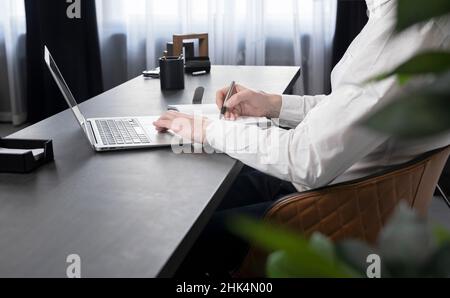 Businessman hands taking notes in notebook and surfing information on Internet or preparing for corporate event or studying distantly. Online work and education concept. High quality photo Stock Photo