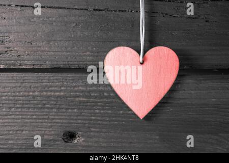 Pink heart shape hanger on a dark rustic wood wall, symbol of love in everyday life and holidays like valentines, mother's day, father's day and birth Stock Photo