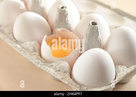 Raw eggs in a cardboard box, one is broken and shows the egg yolk, concept for baking, cooking and Easter, close up shot, selected focus, narrow depth Stock Photo