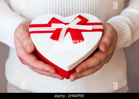 Red heart shaped gift boxt with white bow in man hands. Valentine's day, Birthday, Mother's day or wedding concept. Heart shaped Valentines Day gift b Stock Photo