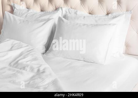Bedroom with bed and white bedding White pillows, duvet and duvet case on bed with beige headboard.  Bed with clean white pillows and bed sheets in be Stock Photo