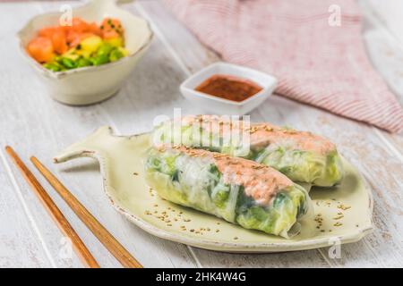 Two summer rolls with salad and salmon and sauce on a white wooden background, japanese, asian food Stock Photo