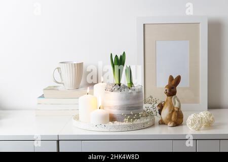 Unblown hyacinths with burning candles on a tray, a stack of books, a mug of tea, a garland of thread on the wall. Easter room decoration. Stock Photo