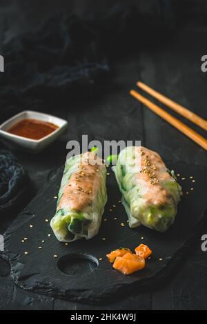 Two summer rolls with salad and salmon on black background, japanese, asian food, vertical Stock Photo