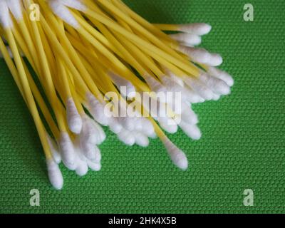 A large number of cotton swabs on a green background, a close-up shot. Cotton swabs or cotton buds. They are most commonly used for ear cleaning. Stock Photo