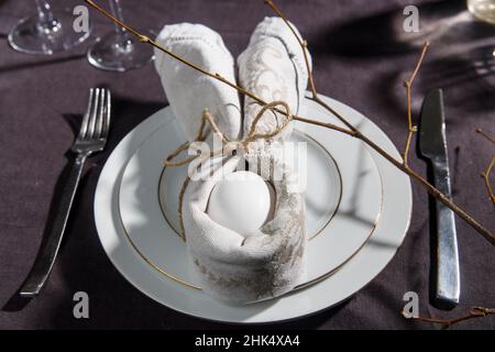 Napkin folder idea. Easter table. Easter holiday table setting with egg in grey napkin Easter Bunny on a brown linen background. Copy space, top view, Stock Photo