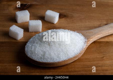 Granulated sugar and sugar cubes in wooden spoon on wooden background Stock Photo