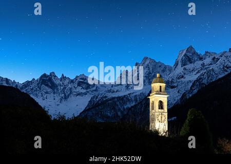 Illuminated bell tower and Sciore mountain range covered with snow under the starry sky, Soglio, Graubunden, Switzerland, Europe Stock Photo