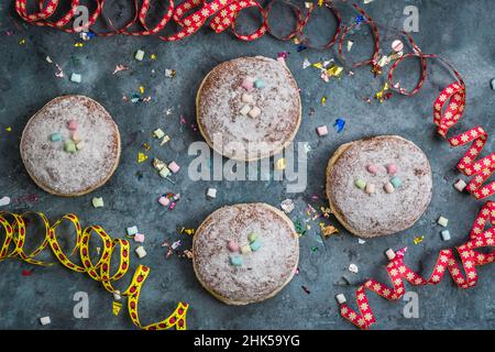 Krapfen, Berliner or donuts with streamers, confetti and mini marshmallows on blue background. Colorful carnival or birthday image, top view Stock Photo