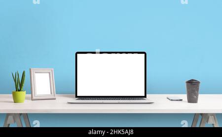 Laptop with blank screen on work desk. Picture frame, plant, coffee and phone beside. Blue wall in background Stock Photo
