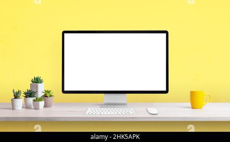 Creative work desk with blank computer display, yellow coffee mug and plants. Yellow background with copy space Stock Photo