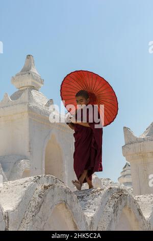 Young novice Buddhist monk holding parasol at Myatheindan Pagoda (also known as Hsinbyume Pagoda), Mingun, Myanmar (Burma), Asia in February Stock Photo
