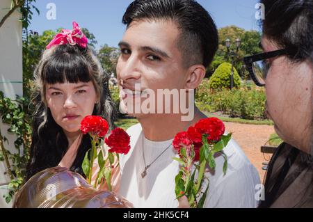 cheating young man on double date outside in public park, with flowers and balloon heart looking at camera with nervous smile, valentine concept Stock Photo