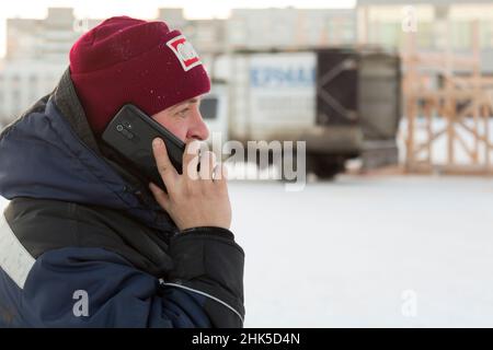 Portrait of an assembler worker in a hooded jacket talking on a mobile ...