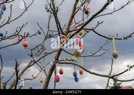 Many Easter eggs decorated outdoor. Handmade diy home exterior decoration with colorful easter eggs hanging on spring branches tree. Creativity craft Stock Photo