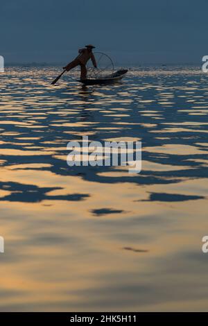 Intha leg rowing fishermen at sun set at Inle Lake, Myanmar (Burma), Asia in February - fisherman standing on one leg rowing with the other Stock Photo