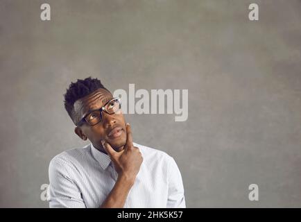 Puzzled confused dark-skinned man looks up and scratches his chin thinking about something. Stock Photo