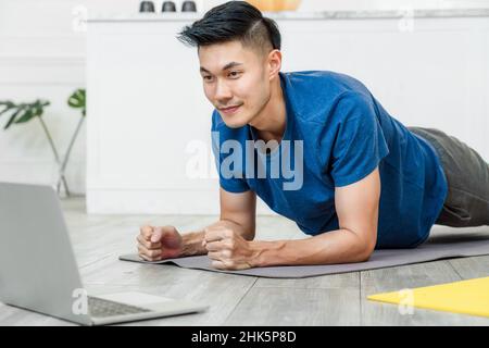 Exercises at home concept, Asian man practicing yoga at home with laptop with planking on the yoga mats Stock Photo