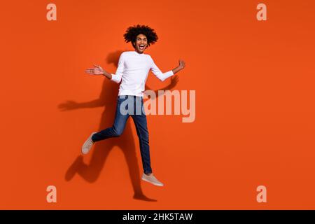 Photo of pretty impressed guy dressed white shirt running fast jumping high empty space isolated orange color background Stock Photo