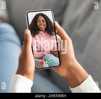 Black lady holding cellphone and making video call with her bestie, resting at home on sofa, closeup, creative collage Stock Photo