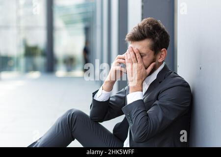 Depressed bankrupt man crying near office outdoors, lost his job and hope Stock Photo