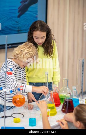 Girl watching boy lowering pipette into flask Stock Photo