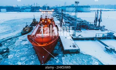 Oil shipment on big red tanker from terminal pumping system on water covered with thick layer of broken ice in frosty winter aerial view Stock Photo