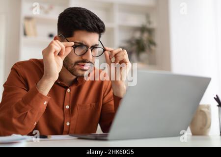 Confused Arab guy using laptop looking at screen Stock Photo