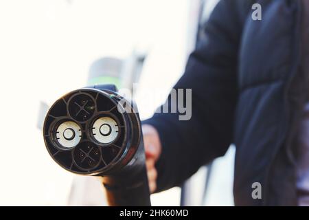 Man holding electric car charger plug type CHAdeMO at charging station with sunflare Stock Photo