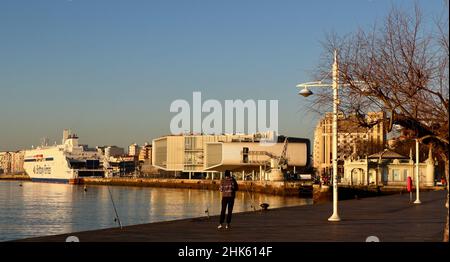 Rod and line fisherman at waters edge Bay of Santander Cantabria Spain with the Salamanca Brittany Ferries ship Stone Crane and Botin Arts Centre Stock Photo