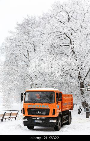 UZHHOROD, UKRAINE - FEBRUARY 2, 2022 - An orange truck is pictured during a snow removal effort by municipal services on the streets in winter, Uzhhor Stock Photo
