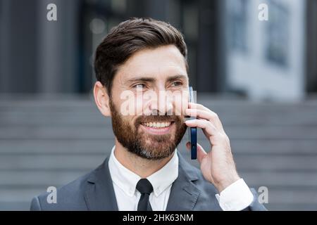 Close-up portrait photo of successful bearded businessman smiling talking on the phone Stock Photo