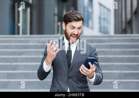 angry male businessman cry talking on the phone outside business man shouting on call outdoors. Nervous mad professional conversation on smartphone. I Stock Photo