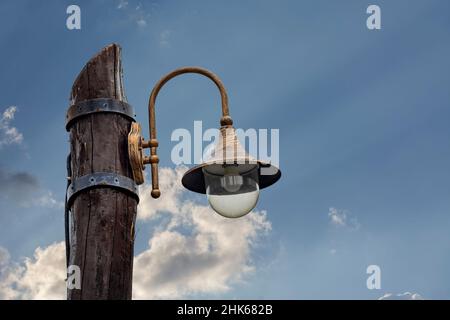 Fragment of a street lamp made in retro style against a blue sky with white clouds. Stock Photo