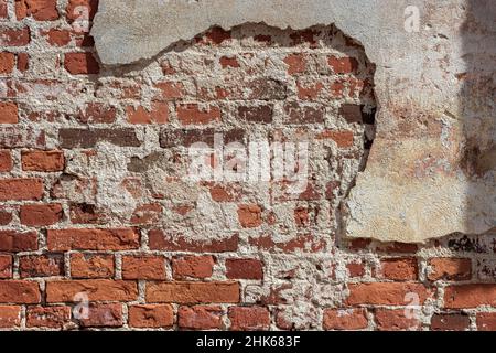 Fragment of a red brick wall partially covered with crumbling plaster for use as an abstract background and texture. Stock Photo