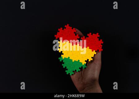 Black History Month background. African American history month celebration. Hand holding heart in red, yellow, green colors flag over black background Stock Photo