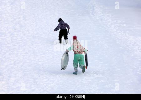 Sledding in winter park, snow weather. Children climb the slide to roll down it Stock Photo