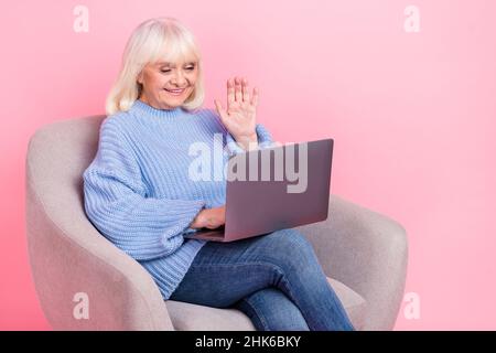 Portrait of attractive cheerful grey-haired woman using laptop calling waving hi hello isolated over pink pastel color background Stock Photo