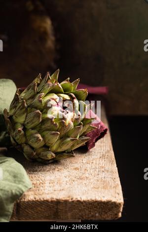 Fresh green artichoke on rustic wooden background with napkins, close up Stock Photo