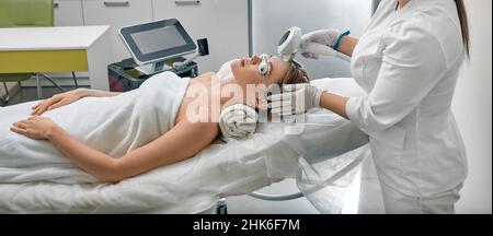 Female patient wearing protective eyeglasses while photorejuvenation procedure with intense pulsed light IPL at medical clinic Stock Photo