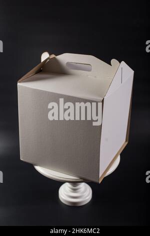 Paper box with blank side on wooden cake stand, on black background. Stock Photo