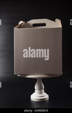 Cake paper box with blank side, on a cake stand on black background. Stock Photo