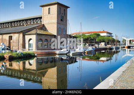 Salt warehouses and boats moored in the colorful canal port of Cervia, Emilia Romagna, Italy Stock Photo
